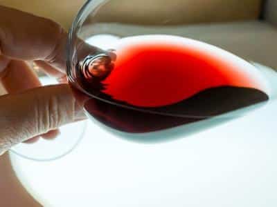 Personne qui analyse les nuances d'un vin rouge dans le verre.